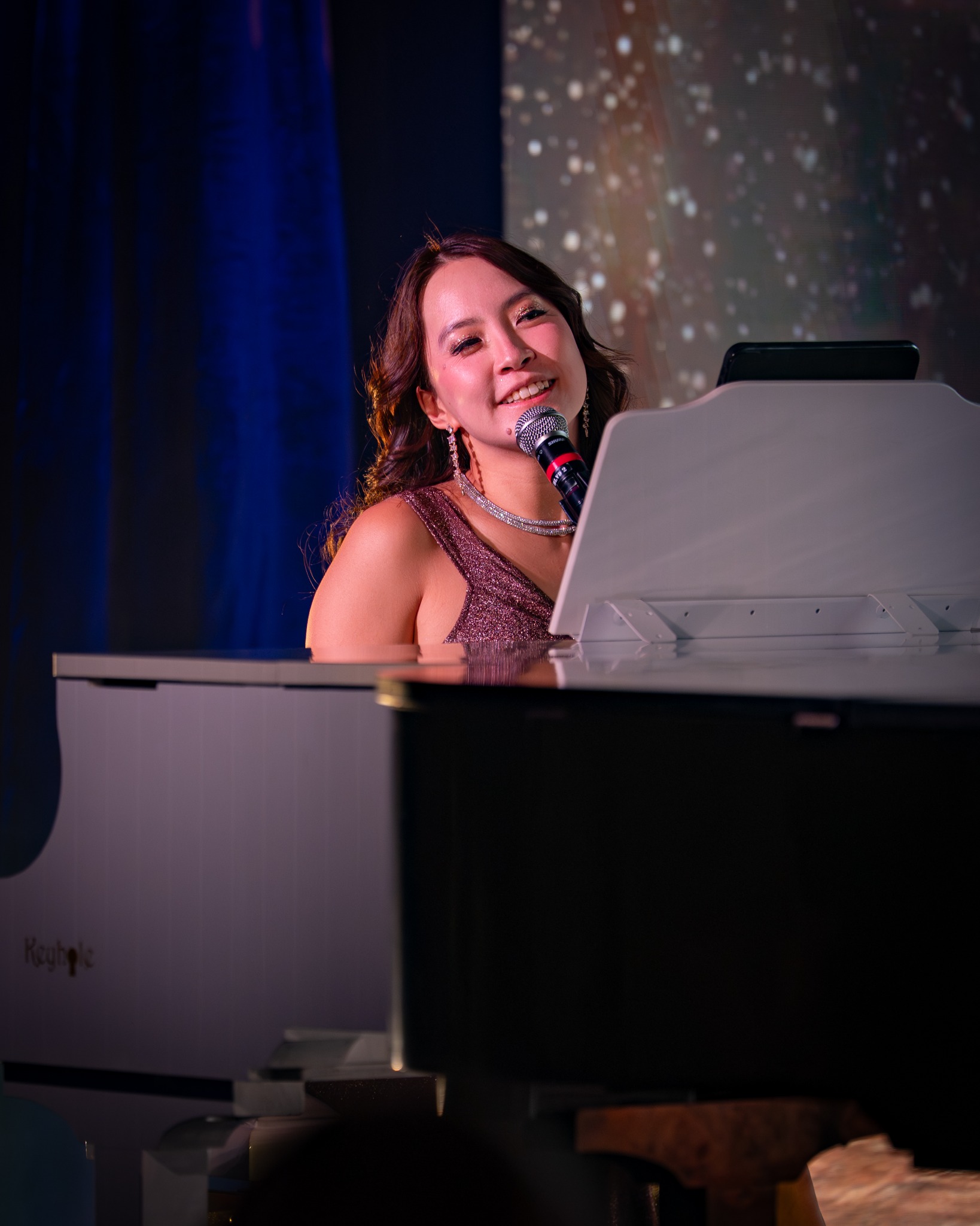 Tammy smiling at the microphone while performing at a white grand piano